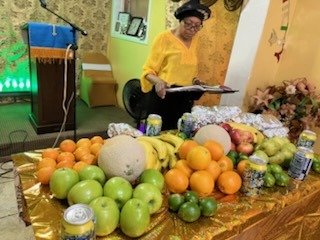 A table laid with fruit at the front of the church while a woman reads at the pulpit