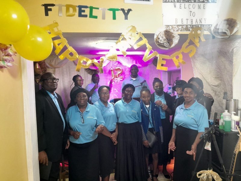 A group from the church in matching light blue shirts beneath a Welcome to Bethany sign